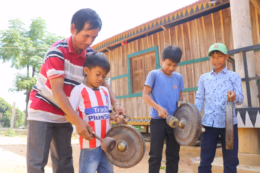 Thiếu niên làng Bờ-Chư Pâu được nghệ nhân trong làng tận tình hường dẫn cách đánh cồng chiêng. Ảnh: Ngọc Minh 