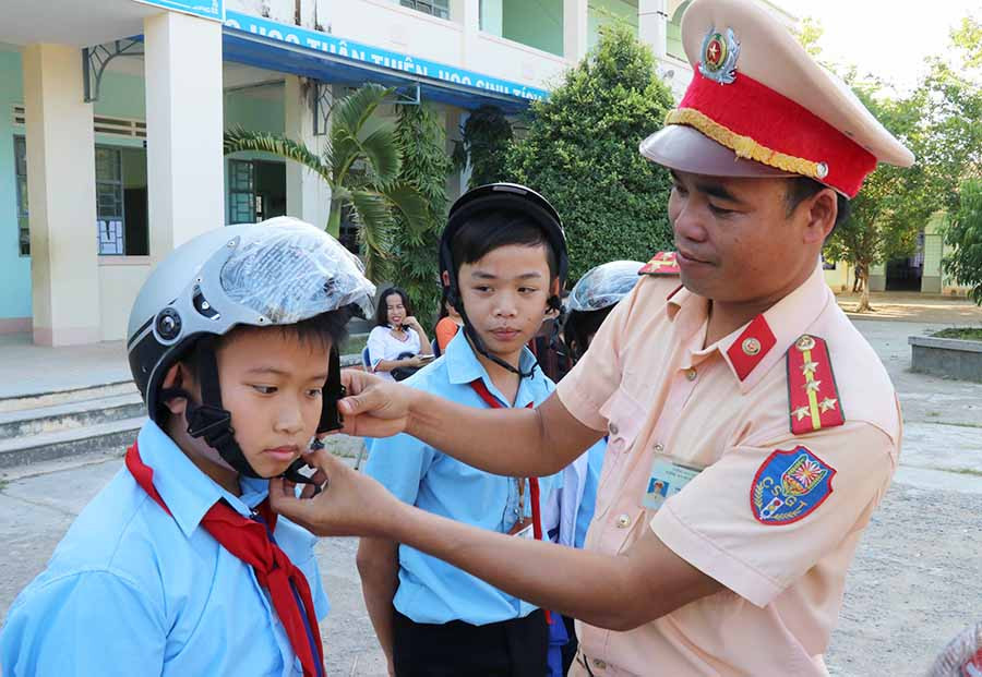  Cán bộ Đội CSGT Công an huyện Phú Thiện hướng dẫn các em học sinh đội mũ bảo hiểm đúng cách. Ảnh: L.V.N