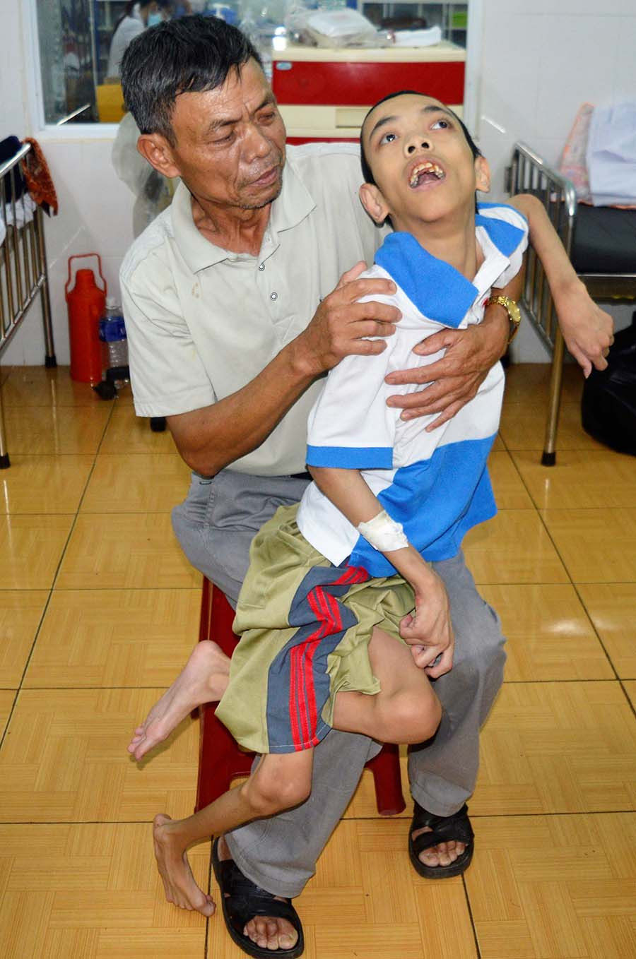  Ông Tùng bên người con bị bại não. Ảnh: H.T