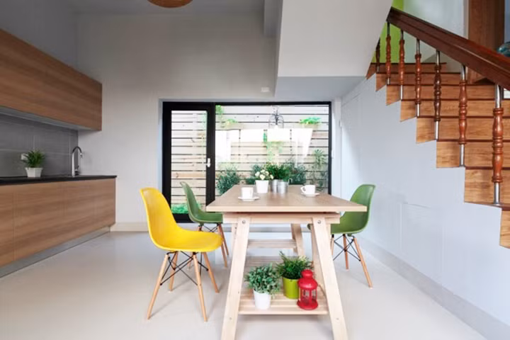 Bàn gỗ, ghế ăn hiện đại đặt cạnh bếp và cầu thang thuận tiện trong việc di chuyển.