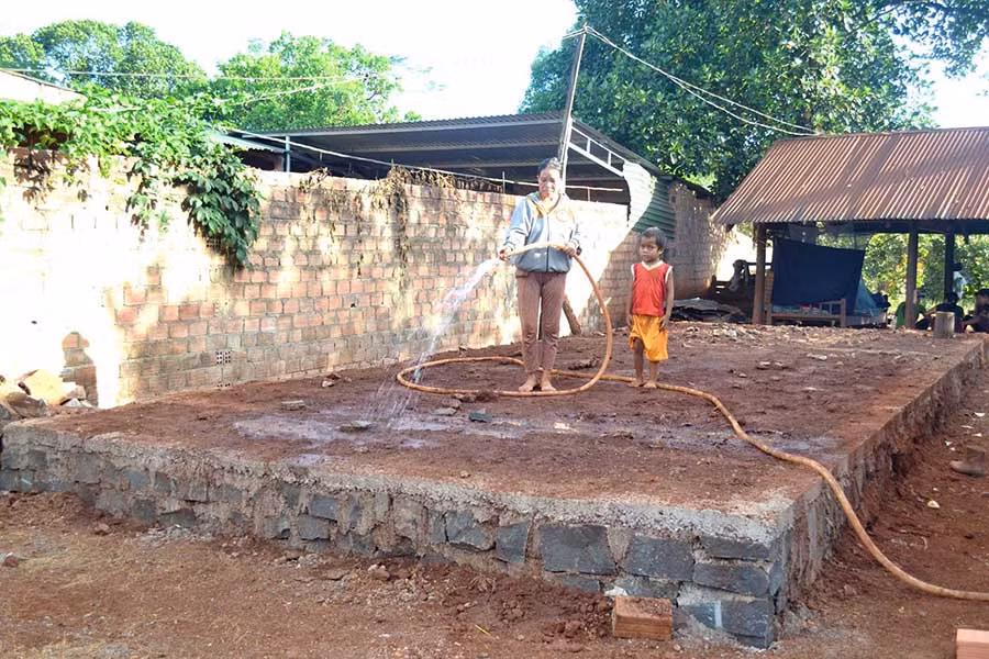  Chị Phyun cùng con út tưới nước cho phần móng ngôi nhà đang thi công. Ảnh: L.H