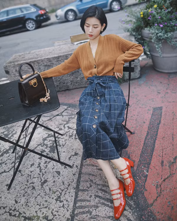 Váy midi thiết kế trên các chất liệu vải kẻ sọc ca rô sử dụng cùng các kiểu áo len, áo nỉ, sweater là công thức lên đồ hài hòa cho quý cô công sở ở mùa thu đông.