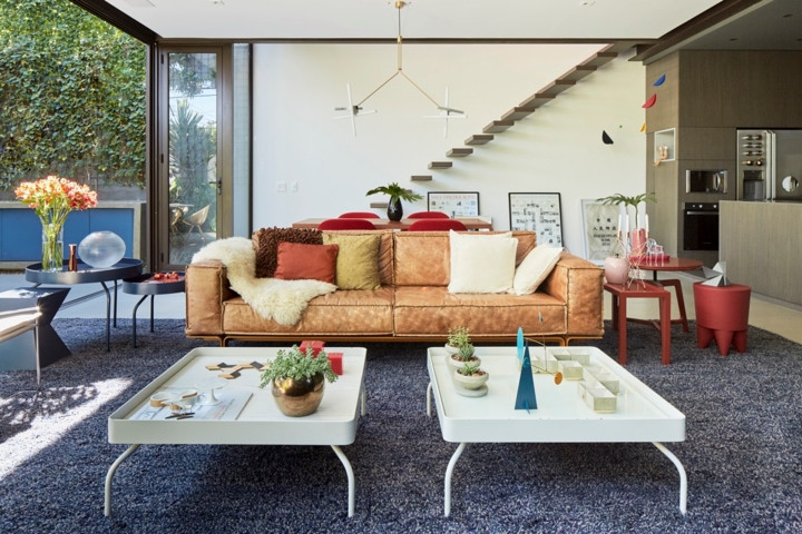 Đồ nội thất tông màu nâu đất phù hợp với các loại cây, trong khi hai bàn cà phê hiện đại màu trắng sắc nét chiếm vị trí trung tâm trong phòng khách. Cầu thang gỗ mang đến một tác phẩm nghệ thuật độc đáo.