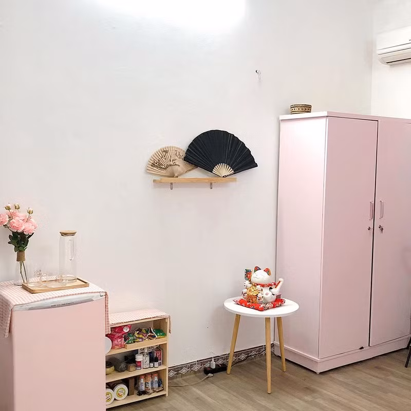 Tủ quần áo mua loại rẻ rồi mua giấy dán tường màu hồng phấn dán lên. Tủ lạnh cũng được dán giấy hồng. Nhà nhiều quạt giấy nên cũng được tận dụng làm đồ trang trí. Chiếc tủ bé để đồ ăn vặt và đồ dùng cá nhân được đặt gọn gàng.