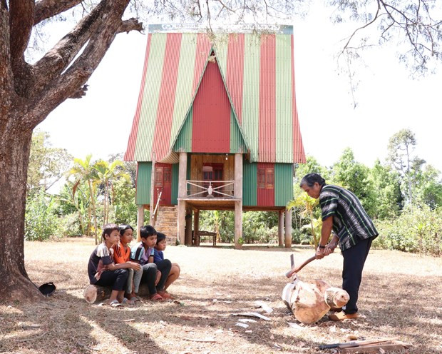 Nghệ nhân ưu tú Ksor Krôh hướng dẫn các em nhỏ tạc tượng gỗ. (Ảnh: Hồng Điệp/TTXVN)