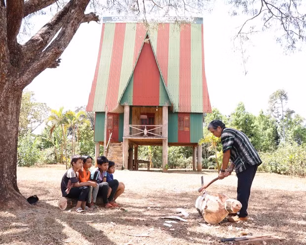 Nghệ nhân ưu tú Ksor Krôh hướng dẫn các em nhỏ tạc tượng gỗ. (Ảnh: Hồng Điệp/TTXVN)