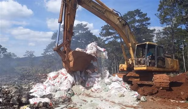 Lực lượng chức năng huyện Bảo Lâm dùng xe cơ giới phá hủy các bao phân bón trước khi chôn lấp để tiêu hủy hoàn toàn. (Ảnh: TTXVN phát)