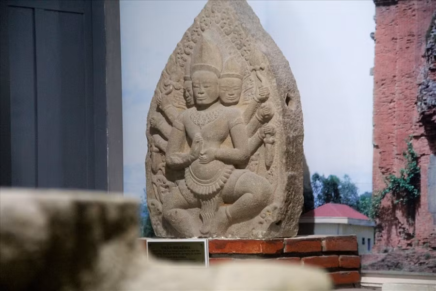 Phù điêu thể hiện thần Brahma trong tư thế nhìn về phía trước, hai chân chùng xuống, hai đầu gối bành ra hai bên, hai tay chính bắt quyết trước ngực. Hai bắp tay, mỗi bên mọc ra thêm ba tay phụ cầm các vật: dao găm, hoa sen. Thần có ba đầu: đầu chính giữa nhìn thẳng, hai đầu hai bên như cố nhô ra để nhìn ra phía trước, cả ba khuôn mặt đều vuông vức, tỏ ra nghiêm nghị.