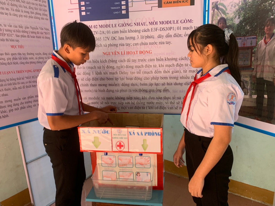 Em Ksor Phương (bìa trái) và Ksor Mai thuyết trình về nguyên lý hoạt động của máy rửa tay không tiếp xúc. Ảnh: Vũ Chi