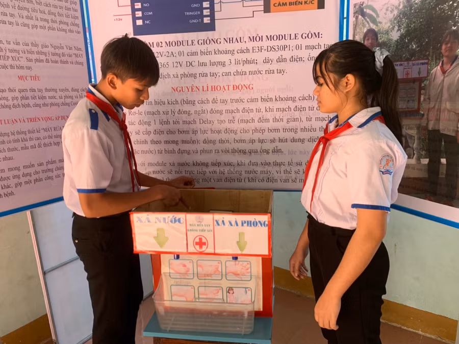 Em Ksor Phương (bìa trái) và Ksor Mai thuyết trình về nguyên lý hoạt động của máy rửa tay không tiếp xúc. Ảnh: Vũ Chi