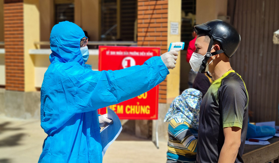 Kiểm tra thân nhiệt người dân người dân đến tiêm phòng vắc xin Covid-19 tại điểm tiêm Trường Tiểu học Trần Quốc Toản (phường Diên Hồng, TP. Pleiku). Ảnh: Bá Bính