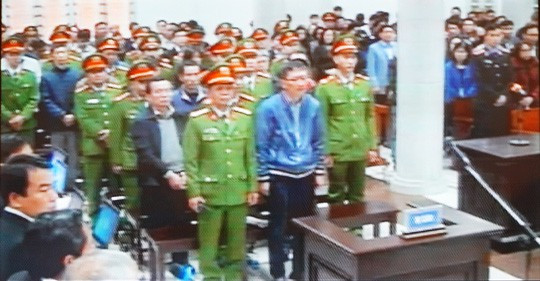 Bị cáo Trịnh Xuân Thanh (áo blu-dông xanh đứng hàng đầu) và các bị cáo khác tại phiên tòa. Theo quy định mới có hiệu lực từ ngày 1-1-2018, các bị cáo đứng khai báo trước bục khai báo thay cho vành móng ngựa trước đây.