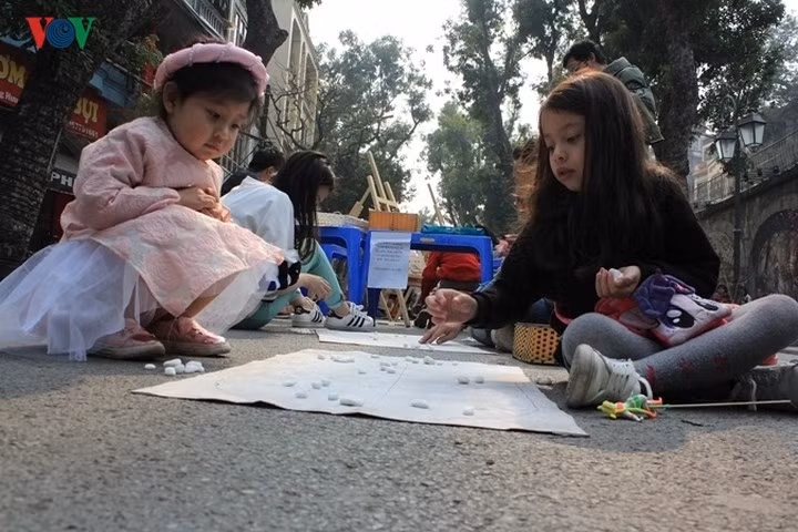 Nhiều em nhỏ xúng xính cùng những bộ áo dài đủ màu sắc đi cùng bố mẹ ra các điểm vui chơi để thưởng thức không khí xuân đang về tại Thủ đô.