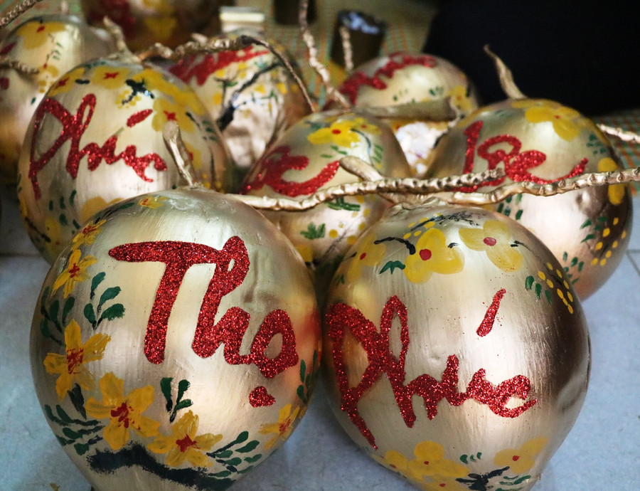 Những quả dừa phun nhũ vàng óng ánh, chữ thư pháp màu đỏ mềm mại lướt trên thân dừa cùng những họa tiết cánh đào, hoa mai xung quanh. Ảnh: Trần Dung Những quả dừa phun nhũ vàng óng ánh, chữ thư pháp màu đỏ mềm mại lướt trên thân dừa cùng những họa tiết cánh đào, hoa mai xung quanh. Ảnh: Trần Dung