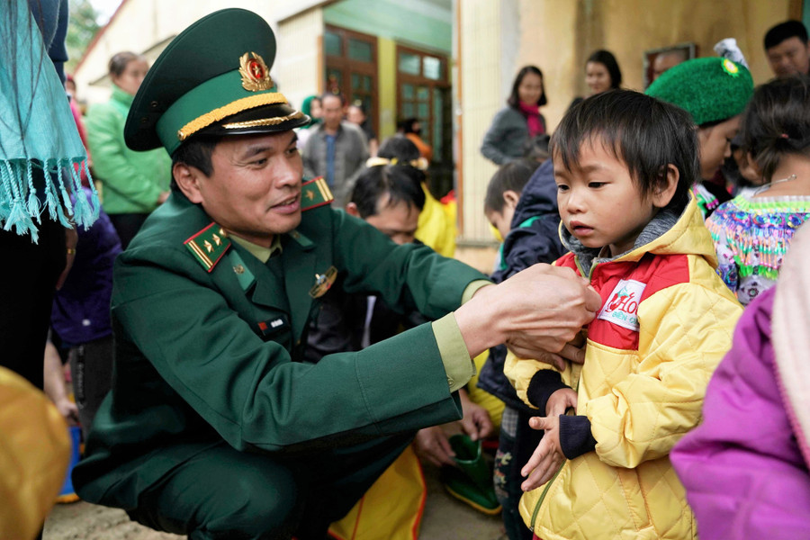 Thượng tá Bùi Văn Huân (Phó trưởng phòng Phòng chống ma túy và tội phạm, BĐBP Hà Giang) cùng cán bộ chiến sĩ Đồn BP Nghĩa Thuận tặng áo ấm cho trẻ em biên giới Quản Bạ. Ảnh: Mai Thanh Hải