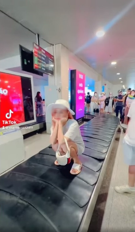 Hình ảnh cô gái trẻ ngồi trên băng chuyền hành lý đang chuyển động tại sân bay ở Việt Nam. Ảnh cắt từ clip