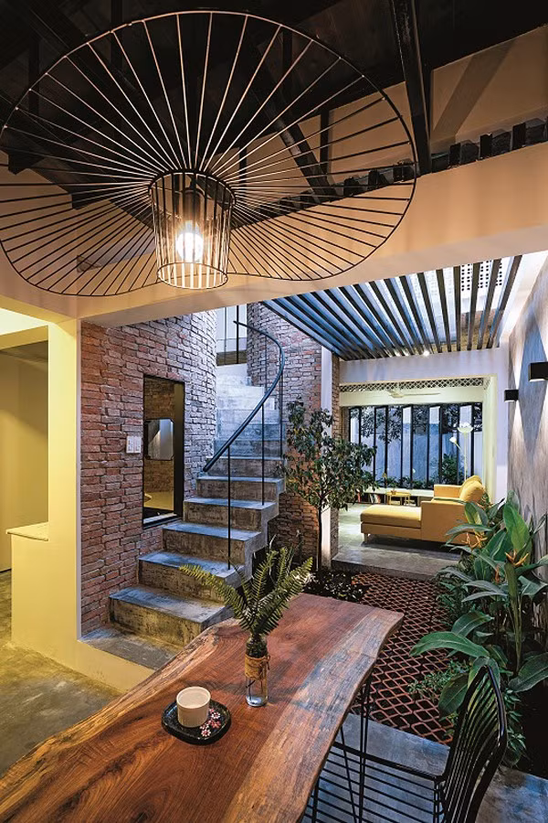 Phòng ăn cũng không có cửa, mở ra khoảng sân trời. Chiếc bàn ăn cũng theo phong cách thô mộc với mặt bàn là một tấm gỗ tự nhiên giản dị. Chiếc đèn bàn ăn là một sản phẩm tự chế từ thép xây dựng.