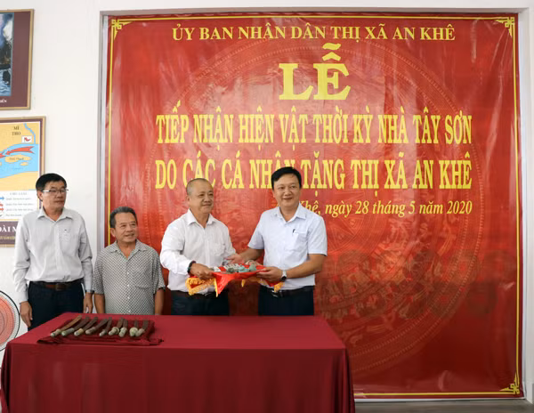 Ông Lâm Dũ Xênh (thứ 3 bên trái_ huyện Bình Sơn, tỉnh Quảng Ngãi) trao tặng 99 đồng tiền và 8 cái lục lạc đồng thời kỳ nhà Tây Sơn cho thị xã An Khê. Ảnh: N.M