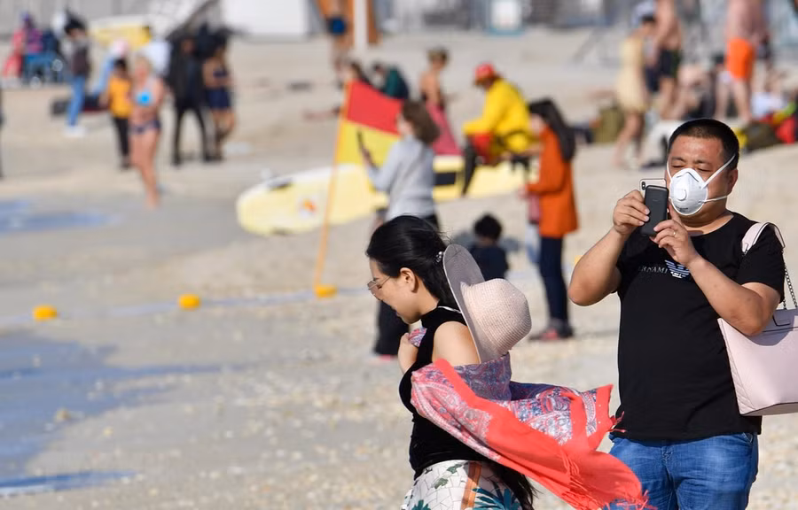 Khách du lịch đeo khẩu trang vui chơi trên bãi biển Dubai, UAE. (Ảnh: AFP/TTXVN)