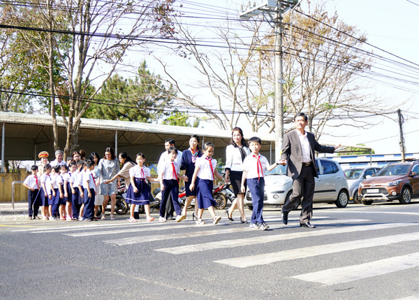 Thành viên Ban An toàn Giao thông tỉnh, đại diện Dự án “Giảm tốc độ-Trường học an toàn” hướng dẫn học sinh Trường Tiểu học Phan Đăng Lưu (TP. Pleiku) qua đường an toàn. Ảnh: L.H