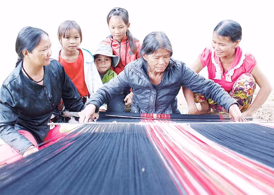 Bà Đinh Thị Gép-con dâu nuôi của ông Phạm Hồng-chỉ dạy con cháu cách dệt thổ cẩm. Ảnh: H.T