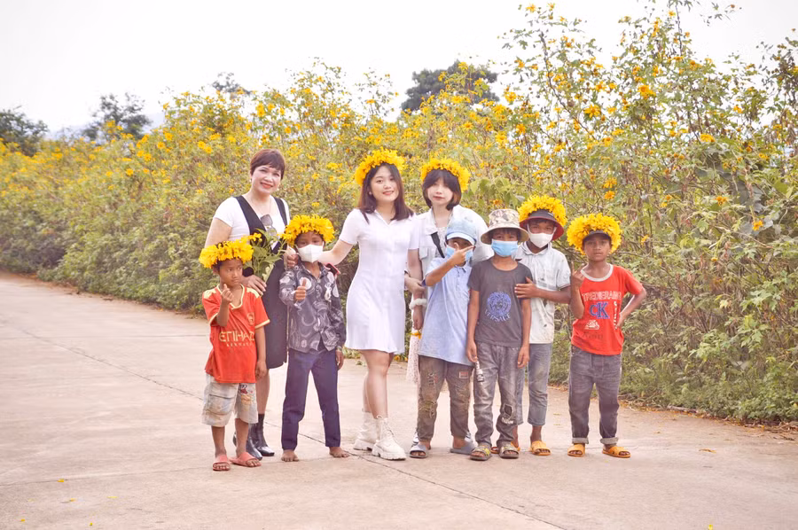 Du khách chụp ảnh cùng các em bé bán vòng nguyệt quế đội đầu được kết từ hoa dã quỳ ở Chư Đang Ya. Ảnh: Hải Lê