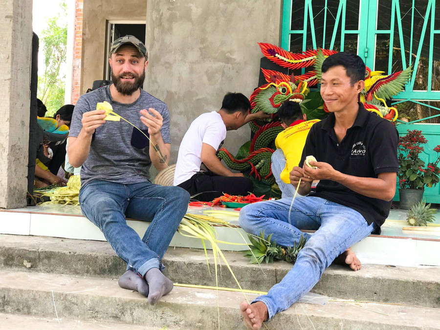 Một người nước ngoài thích thú trải nghiệm làm cổng cưới truyền thống cùng anh Tâm. Ảnh: Duy Tân