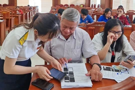 Công chức ngành Thuế tỉnh hỗ trợ hộ kinh doanh chuẩn bị chuyển thành DN cài đặt ứng dụng nộp thuế điện tử trên thiết bị điện thoại di động. Ảnh: T.Sỹ