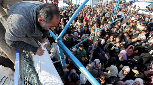Người đàn ông Palestine nhận hỗ trợ trong khi những người khác chờ đến lượt mình. Ảnh: Reuters