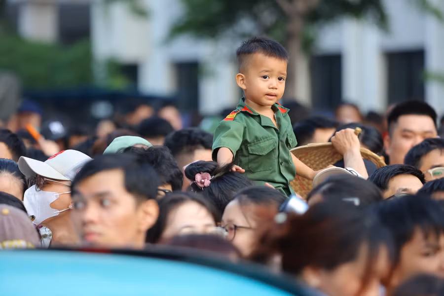Những em bé được bố mẹ cõng trên lưng, hòa vào không khí đông đúc và đầy tự hào giữa biển người khu vực đường Lê Duẩn, hướng ra trục Lê Lợi - Nam Kỳ Khởi Nghĩa.