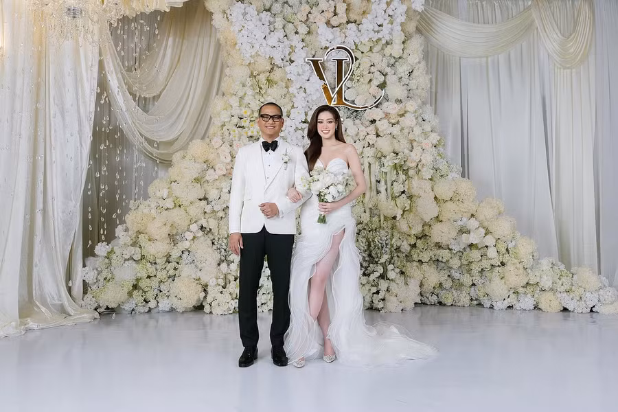 Lễ cưới của Hoa hậu Khánh Vân và nhiếp ảnh gia Long Nguyễn diễn ra tối 12/12 tại TPHCM. Khánh Vân váy cúp ngực, chân váy xẻ cao đón khách, chú rể diện âu phục tông đen trắng. Không gian tiệc cưới trang trí nhiều hoa tươi với tông màu trắng chủ đạo.