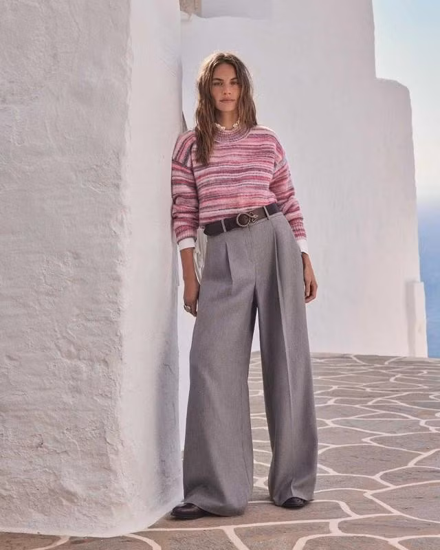 Quần tây ống rộng màu xám phối sơ mi trắng, áo len kẻ sọc tông hồng tươi tắn và dây lưng da tạo nên hình ảnh phóng khoáng và lịch thiệp