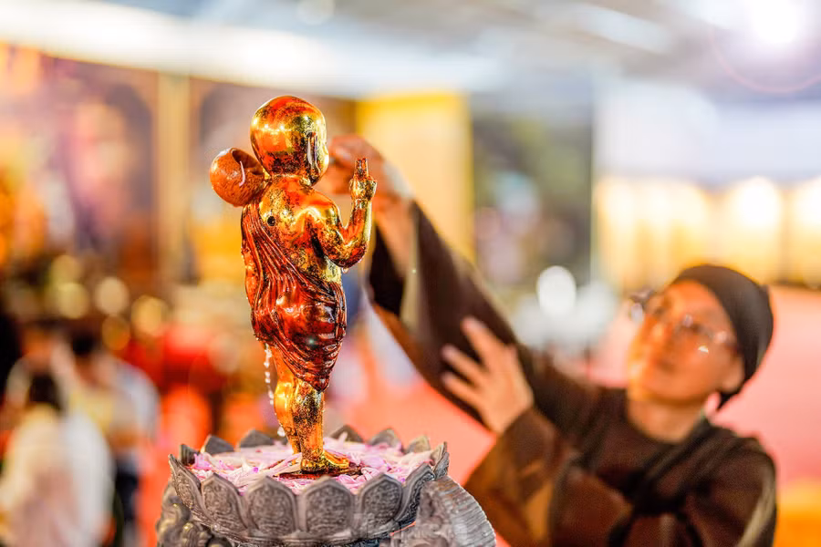 Một cư sĩ đang thực hiện nghi thức tắm Phật trong không gian triển lãm.