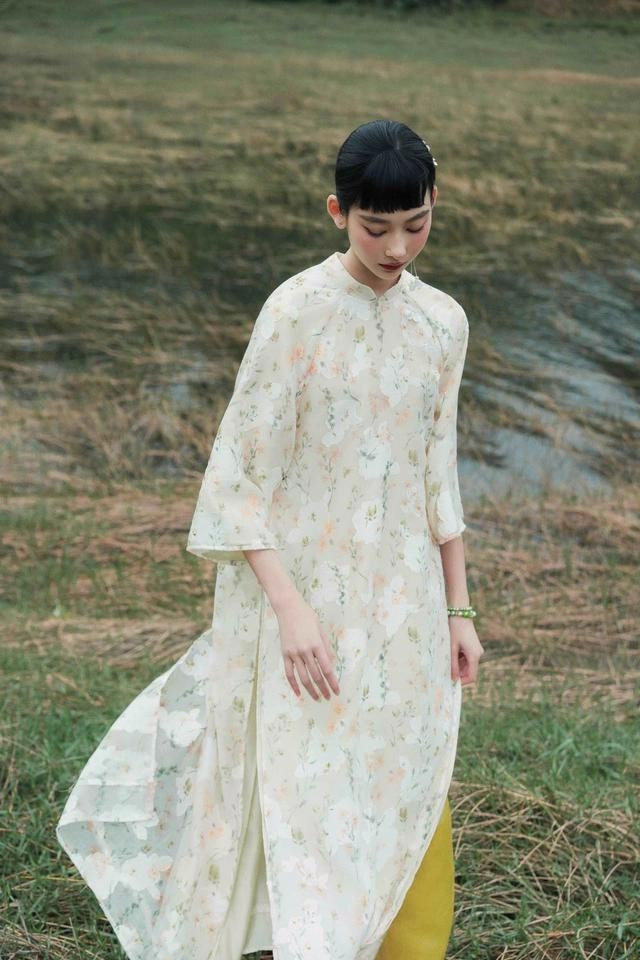 Họa tiết hoa cỏ đan xen trên gam màu mát dịu của áo dài tay lỡ, cổ thấp nhẹ nhàng tôn lên đường nét thanh mảnh nơi vai, cổ