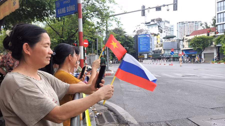 Người dân Hà Nội cầm cờ Việt Nam và Nga chờ đón đoàn xe chở Tổng thống Putin đi qua. (Ảnh: Phạm Duy)