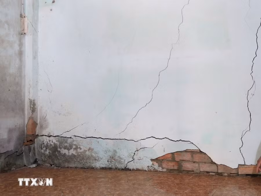 Tường của nhiều ngôi nhà bị nứt, hư hỏng do ảnh hưởng của việc tuyến đường bên trên sụt lún, sạt trượt. (Ảnh: Minh Hưng/TTXVN)