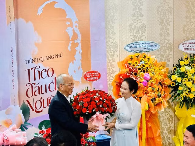 Nhà văn Bích Ngân, Chủ tịch Hội Nhà văn TP HCM (phải), tặng hoa chúc mừng nhà văn Trình Quang Phú dịp ra mắt sách “Theo dấu chân Người”