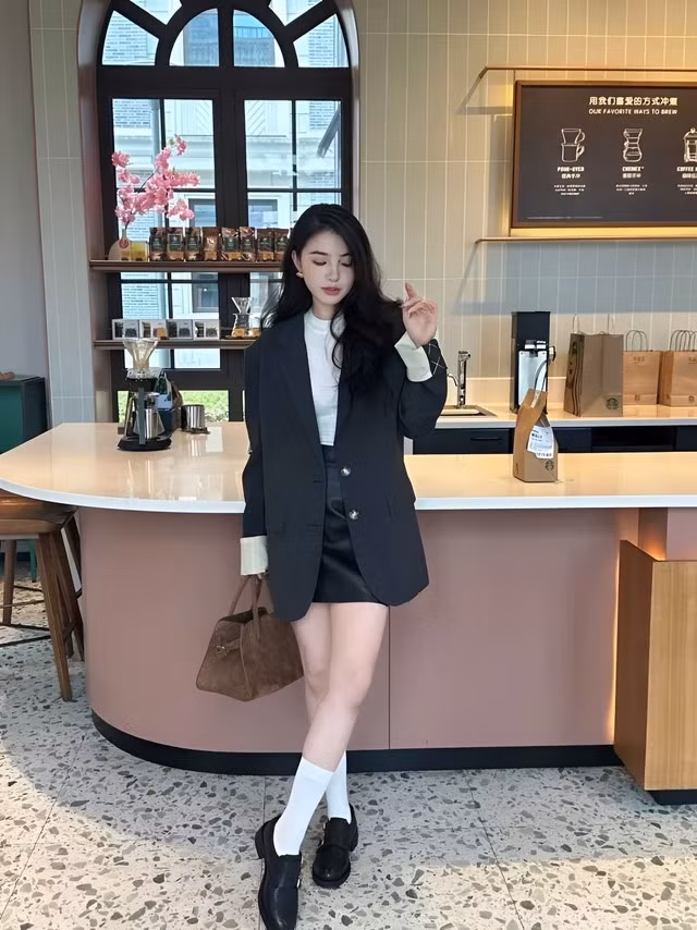Áo blazer xám tro phom rộng mặc ngoài áo thun trắng và chân váy da ngắn màu đen, phối cùng giày oxford và tất trắng tạo nên diện mạo hiện đại. Ảnh: CARDINA