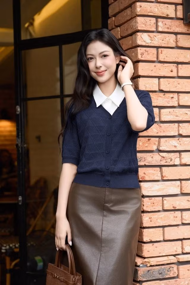 Chân váy da suông midi màu nâu cà phê có đường xẻ nhẹ sau lưng giúp bước đi thêm phần thanh thoát. Nàng kết hợp cùng áo cardigan dệt kim mỏng màu be cát hoặc xanh navy sẫm, layer bên trong là áo sơ mi trắng cổ bẻ nhọn thanh lịch. Ảnh: CARDINA