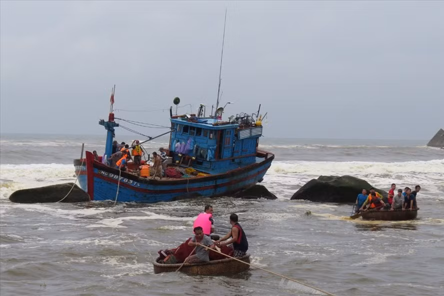 Lực lượng chức năng cùng ngư dân đang cứu nạn tàu cá bị sóng xô vào đá ở cửa biển Mỹ Á.
