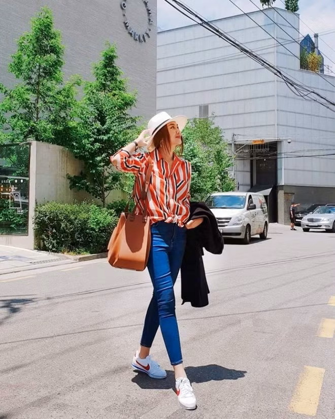  Thanh Hằng khoe dáng nuột nà với quần jeans cạp cao và sơ mi kẻ sọc màu nổi. Đôi giày thể thao cùng mũ cói vành tròn là cặp phụ kiện hoàn hảo, vừa giúp siêu mẫu che nắng lại thoải mái di chuyển khi tản bộ trên những con phố tại Hàn Quốc. Và tất nhiên, chiếc túi Hammock từ Loewe – “bảo bối” yêu thích của người đẹp cũng đồng hành trong chuyến đi này.