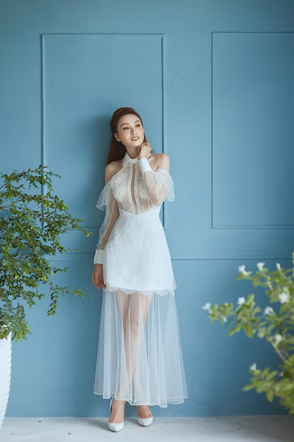 Đầm khoét vai thêm phần gợi cảm nhờ cách phối hợp khéo léo các chất liệu vải xuyên thấu, vải ren và lụa đồng sắc trắng.