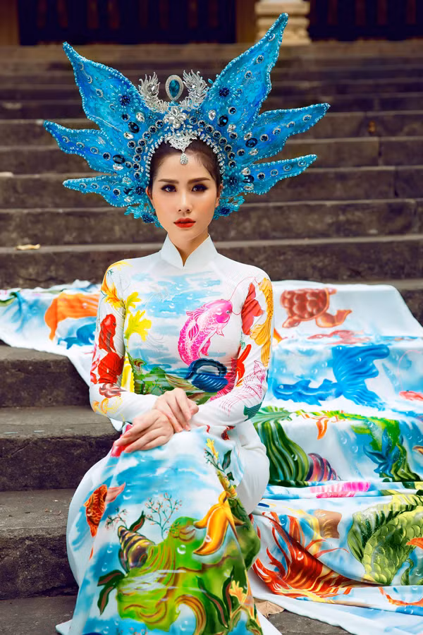  Phom áo dài dáng truyền thống nhưng lại gây ấn tượng mạnh bằng chi tiết đuôi váy dài hoặc tà áo rộng, thể hiện vẻ quyền lực. Nhà thiết kế còn kỳ công làm chiếc vương miện độc đáo, được đính kết từ nhiều viên pha lê. 