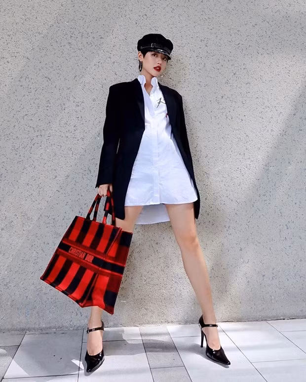  Khánh Linh phô diễn đôi chân thon dài với combo sơmi và blazer dáng rộng, mix theo công thức giấu quần. Điểm sáng của bộ cánh tối giản chính là chiếc túi Book Tote kẻ sọc đỏ đen của Dior.