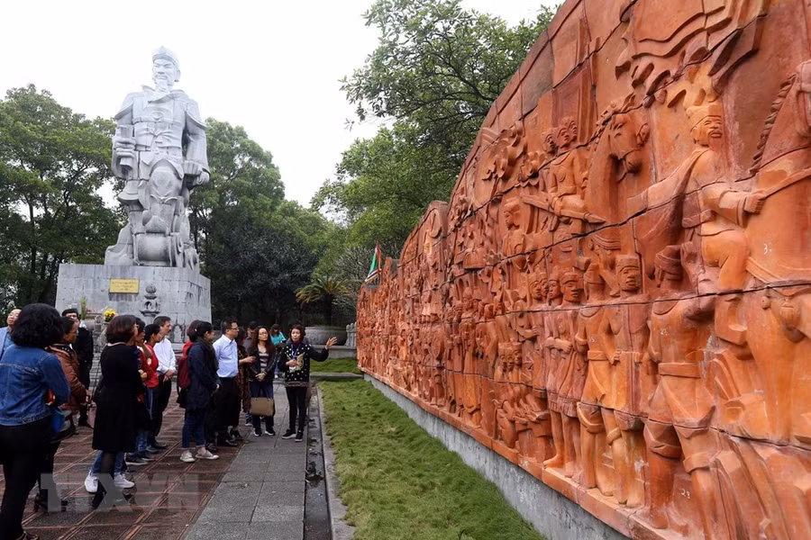 Du khách tham quan bức phù điêu ghi lại chiến công lịch sử được làm bằng đất nung cạnh Tượng đài Hưng Đạo Vương Trần Quốc Tuấn trong quần thể Đền Cao An Phụ.