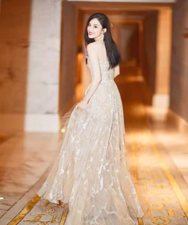 Viền váy dài mềm mại, thướt tha, thanh thoát, vạt váy nhẹ được trang trí bằng nhiều dây buộc nấm, toát lên vẻ ngọt ngào và khí chất thần tiên. Váy được đính sequins ngọc trai tinh xảo, lấp lánh dưới ánh đèn. Nâng gấu váy, Cổ Lực Na Trát bước trên đôi giày cao gót màu vàng sâm panh sáng bóng và di chuyển, tinh tế và trang nhã lộ ra vẻ lộng lẫy cùng nụ cười ngọt ngào làm 