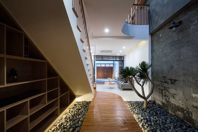 Giữa nhà có khoảng đệm là vườn sỏi với cây phát tài thích hợp với điều kiện ít ánh sáng. Gầm cầu thang cũng được tận dụng để kê một hệ tủ chạy dài.
