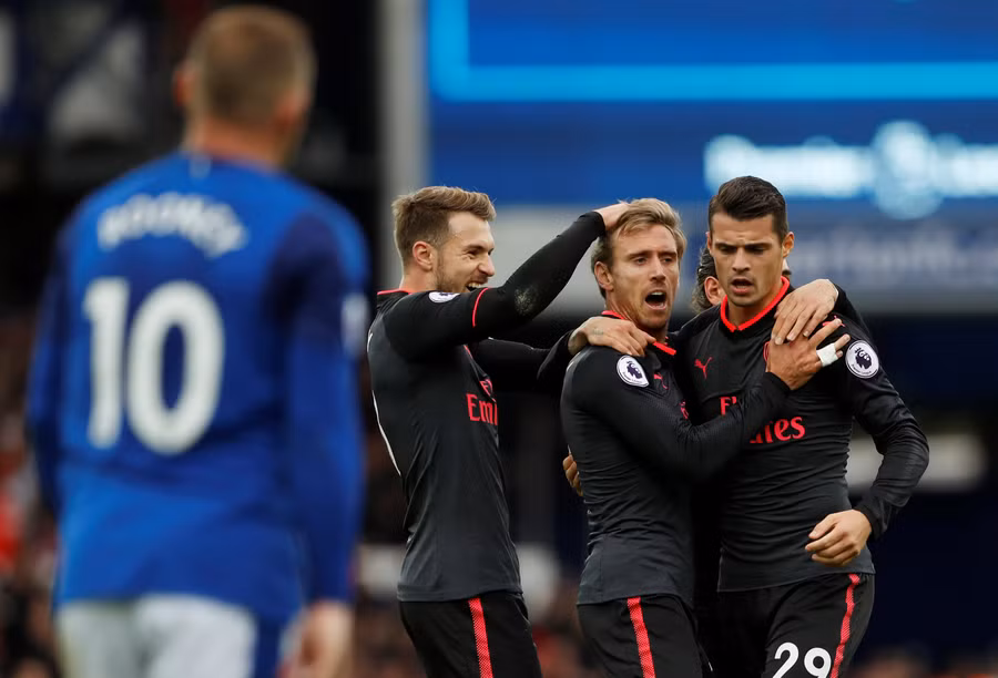 Niềm vui của các cầu thủ Arsenal sau khi Monreal gỡ hòa 1-1. Ảnh: REUTERS Rooney (trái) ăn mừng bàn mở tỉ số cho Everton. Ảnh: GETTY IMAGES