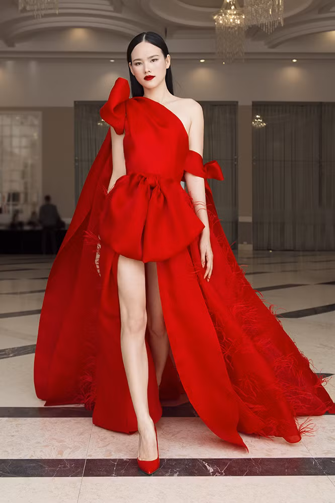  Cụ thể, Á quân Vietnam’s Next Top Model 2010 đã lựa chọn bộ đầm có thiết kế lệch vai tông màu đỏ bắt mắt, với chất liệu chính là organza và lông vũ.