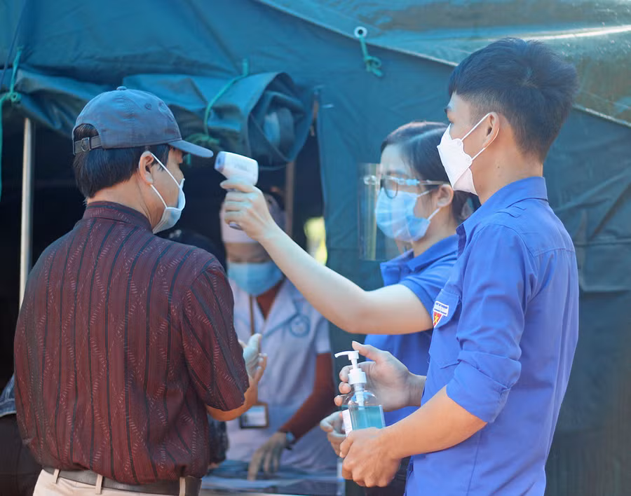Tình nguyện viên của Thành Đoàn Pleiku hỗ trợ đo thân nhiệt người dân đến khám bệnh tại Trung tâm Y tế TP. Pleiku. Ảnh: Phan Lài